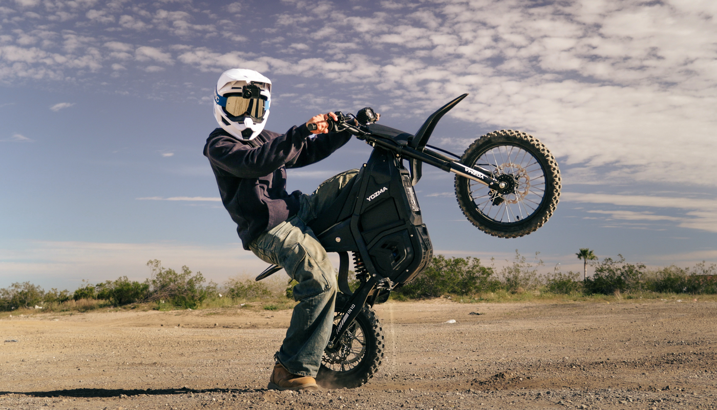 Rider performing wheelie on Yozma IN10 electric dirt bike at sunset